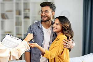 Real estate agent giving keys to young indian buyers, happy woman taking key of future new apartment, spouses buying new house