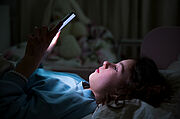 A child using smart phone lying in bed late at night, playing games, watching videos online, scrolling screen. Children's screen addiction and parent control concept. Child's room at night.