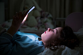 A child using smart phone lying in bed late at night, playing games, watching videos online, scrolling screen. Children's screen addiction and parent control concept. Child's room at night.