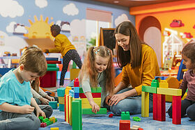 Happy Kindergarten Pedagogue Having a Conversation with Kids, Using Enthusiastic Teaching Methods in a Modern Colorful Kindergarten. Female Educator Stimulating Linguistic and Social Skills